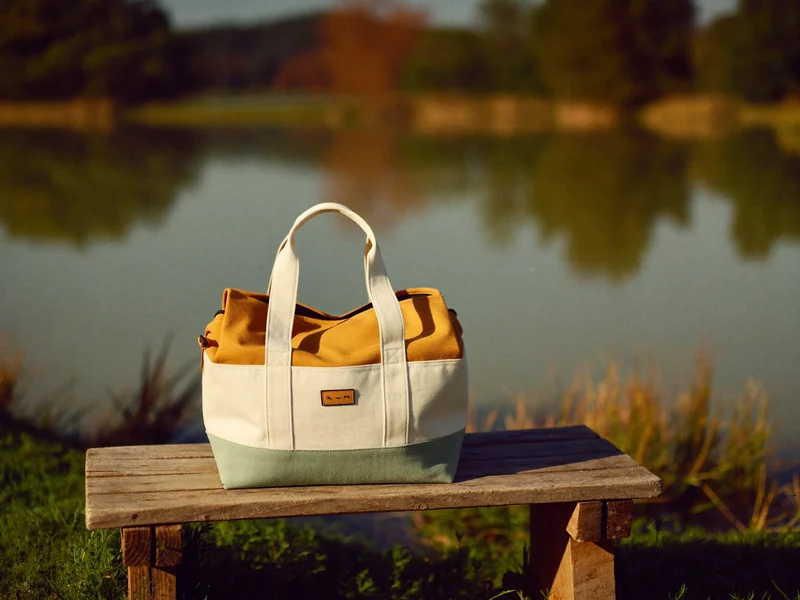 Sac isotherme en toile et coton ciré debout sur un banc en bois au bord d'un lac